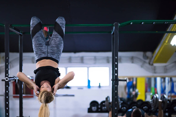 athlete woman doing abs exercises hanging upside down on horizontal bar at cross fitness gym - Foto, immagini