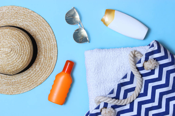 пляжная сумка с пляжными аксессуарами на цветном фоне вид сверху. солнцезащитный крем, полотенце, очки, шляпа
. - Фото, изображение