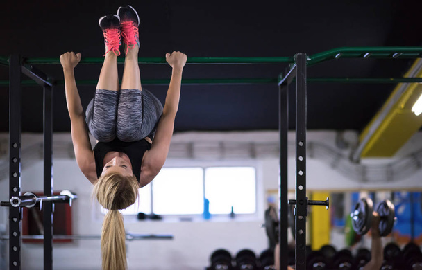 athlete woman doing abs exercises hanging upside down on horizontal bar at cross fitness gym - Foto, Imagen