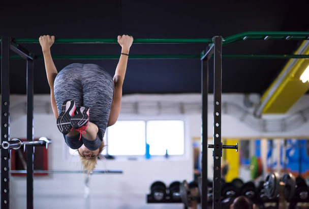 athlete woman doing abs exercises hanging upside down on horizontal bar at cross fitness gym - Foto, imagen