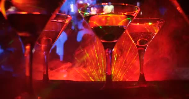 Several glasses of famous cocktail Martini, shot at a bar with dark toned foggy background and disco lights. Club drink concept. Selective focus - Footage, Video