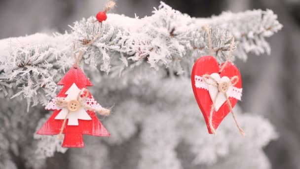 Красные деревянные рождественские игрушки сердце и елка висят на ветвях снежной елки. Видеодвижение
 - Кадры, видео