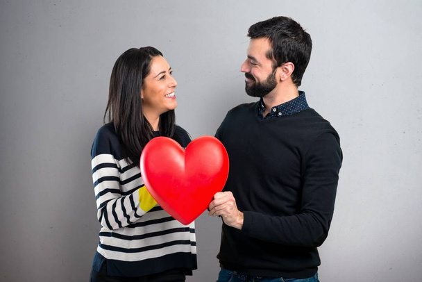 Ζευγάρι κρατώντας ένα παιχνίδι καρδιά σε γκρίζο φόντο - Φωτογραφία, εικόνα