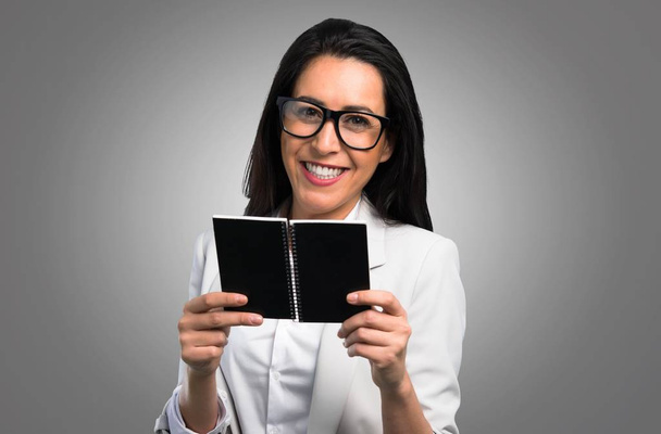 Όμορφη γυναίκα με γυαλιά κρατώντας ένα σημειωματάριο σε γκρίζο φόντο - Φωτογραφία, εικόνα