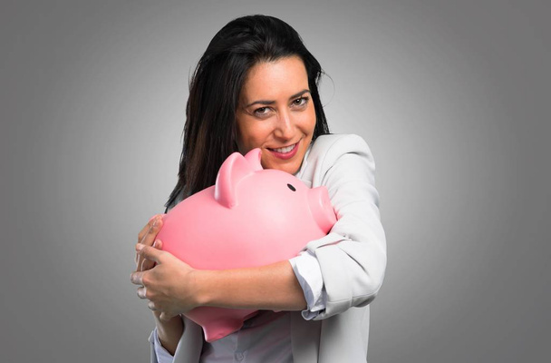 Pretty woman holding a piggybank on grey background - Photo, Image