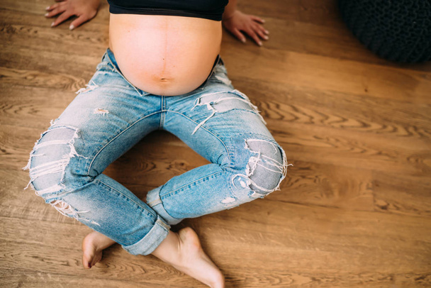 Close up details of baby bump - pregnant woman sitting on hardwood floors - Foto, imagen