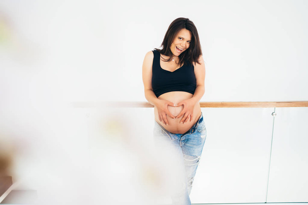 Pregnant woman in new home holds hands on belly on a white background - Fotoğraf, Görsel