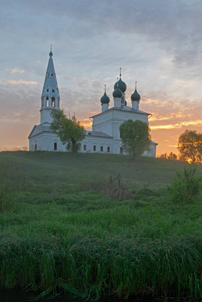 Sonnenaufgang im winzigen Dorf osenevo. Kasanska-Kirche unter roten Sonnenstrahlen. - Foto, Bild