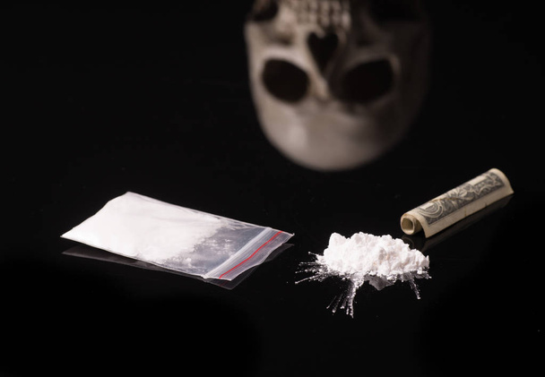 cocaína, Herion ou outras drogas ilegais que são cheiradas por meio de um tubo ou injetadas com uma seringa, dinheiro e Caveira, isoladas em fundo preto brilhante
 - Foto, Imagem