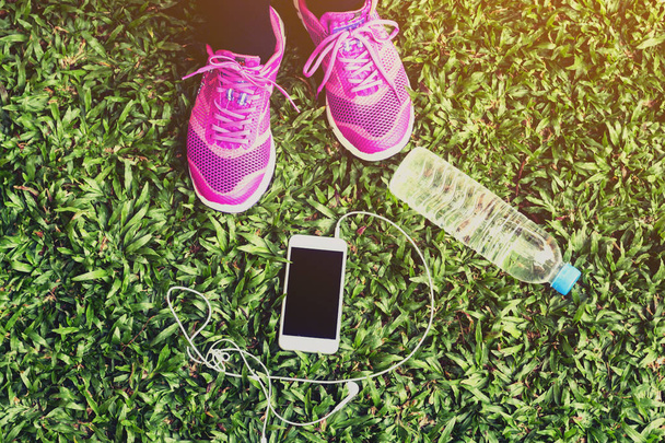 Female runner with smartphone and water bottle on grass - Fotoğraf, Görsel