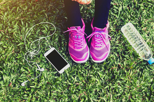 Female runner with smartphone and water bottle on grass - Foto, Imagem