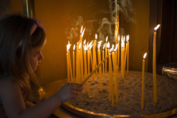 Pieni tyttö rukoilee ja laittaa kynttilän ortodoksiseen kirkkoon
 - Valokuva, kuva