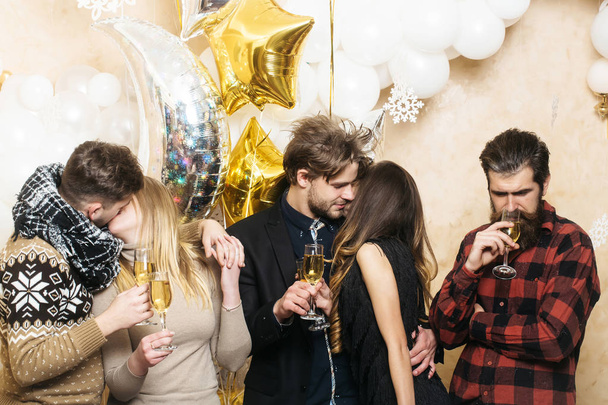 Друзья празднуют Рождество или Новый год, дружбу. Мужчины и женщины пьют шампанское. Пара влюблённых целуются. Мужчины и женщины любят веселиться. Рождество и Новый год
 - Фото, изображение
