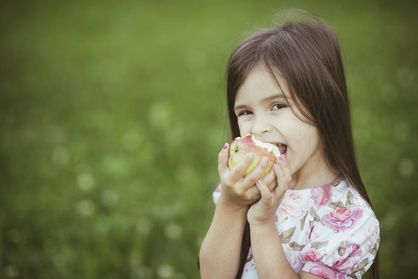 Funny little girl biting apple - Foto, imagen
