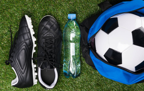 Sapatos e bola para jogar futebol em um gramado verde
 - Foto, Imagem