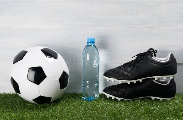 a bottle of water on a green lawn next to the ball and shoes for football - 写真・画像