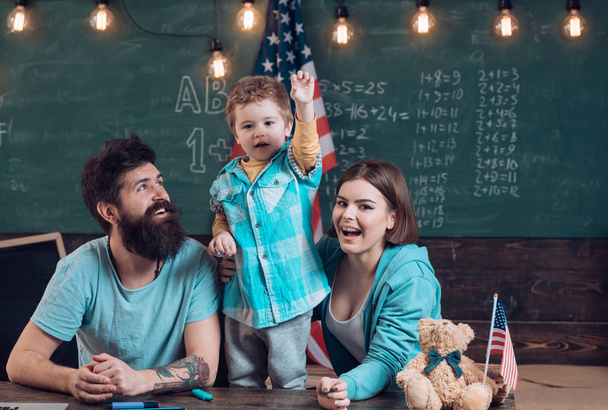 Kid with parents in classroom with usa flag, chalkboard on background. Patriotic education concept. American family sit at desk with son and usa flag. Parents teaching son american traditions playing. - Fotoğraf, Görsel