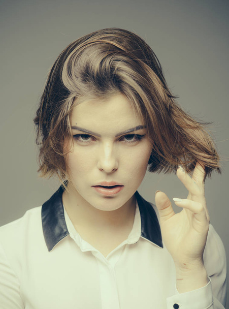 Woman on mysterious face touches her hair, grey background. Girl with fresh haircut, enjoying new hairstyle. Fashion shot of girl with bob haircut . Hairstyle concept. Pretty woman play with hair. - Foto, imagen