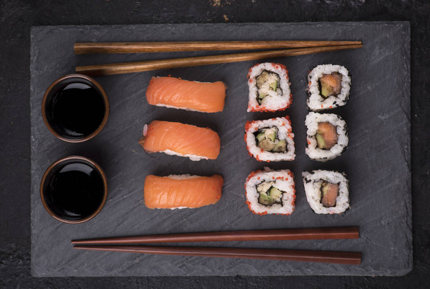 巻き寿司は、上から黒寿司ボードにサーモンとマグロのセット。伝統的な日本料理の平面図です。箸で黒い石スレートのアジア料理. - 写真・画像