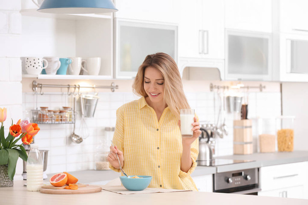 Beautiful young woman having breakfast and drinking milk in kitchen - Foto, afbeelding