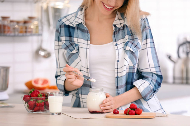 Young attractive woman eating tasty yogurt at table in kitchen - Fotoğraf, Görsel