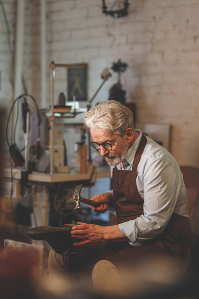Een oudere schoenmaker op het werk in de studio - Foto, afbeelding