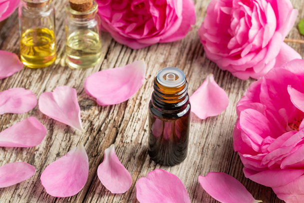 Uma garrafa de óleo essencial com rosas e pétalas frescas sobre um fundo de madeira
 - Foto, Imagem