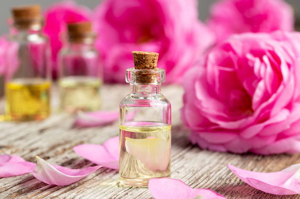 Uma garrafa de óleo essencial com rosas e pétalas frescas sobre um fundo de madeira
 - Foto, Imagem