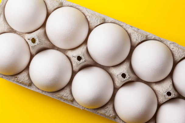 valkoiset raaka munat pakkauksessa keltaisella pohjalla, ylhäältä
 - Valokuva, kuva