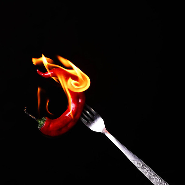 Gabel spießt auf rotem Chili auf schwarzem Hintergrund.  - Foto, Bild