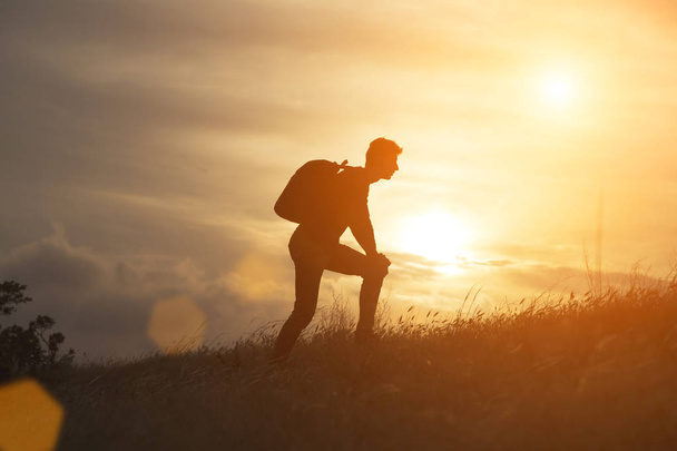 Silhouette de hombre turístico extendido de la mano en la cima de una montaña disfrutando de la puesta de sol. El deporte y el concepto de vida activa - Foto, imagen