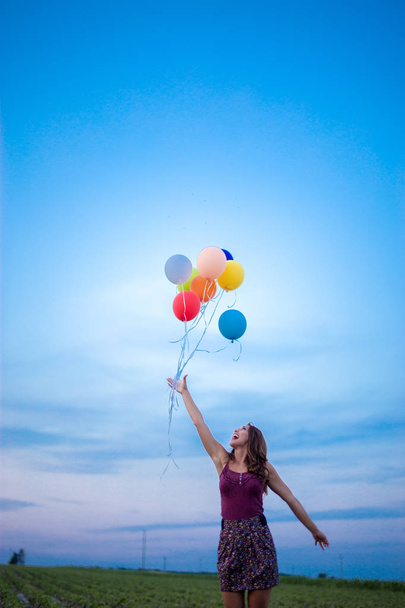 Happy young woman releasing balloons into the sky on a field at sunset - Foto, Bild