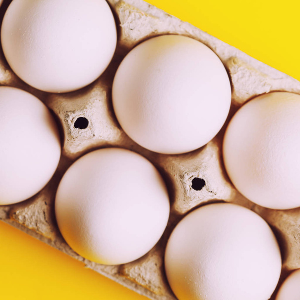 white raw eggs in pack on yellow background, close up - Fotoğraf, Görsel