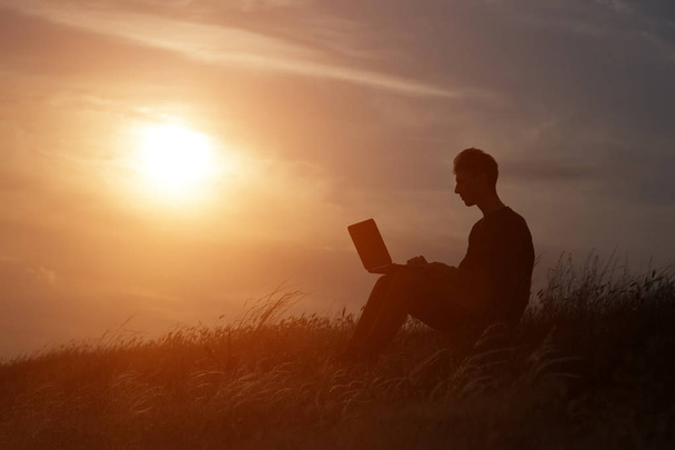 sylwetka szczęśliwego biznesmena z laptopem pracującego na polu o zachodzie słońca - Zdjęcie, obraz