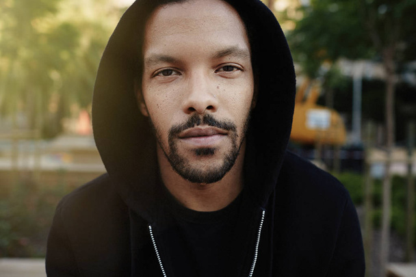 Closeup portrait of confident young African-American man hipster in sport hoody looking at camera.Blurred city on background - Fotografie, Obrázek