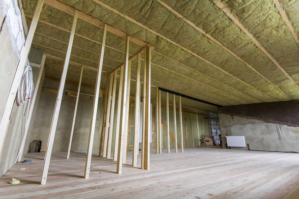 Construction and renovation of big spacious empty unfinished attic room with oak floor, walls and ceiling insulated with rock wool and fiber glass for cold barrier and wooden frame for future walls. - Photo, Image