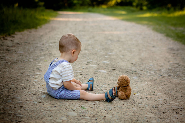 Little boy playing with teddy bear on the footpath. - Zdjęcie, obraz