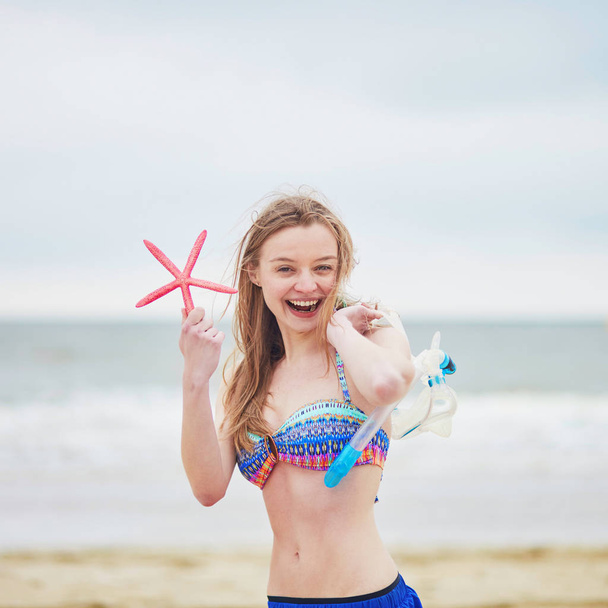 Happy young woman in bikini with snorkelling equipment and pink starfish enjoying summer vacation holidays by ocean or sea - Foto, immagini