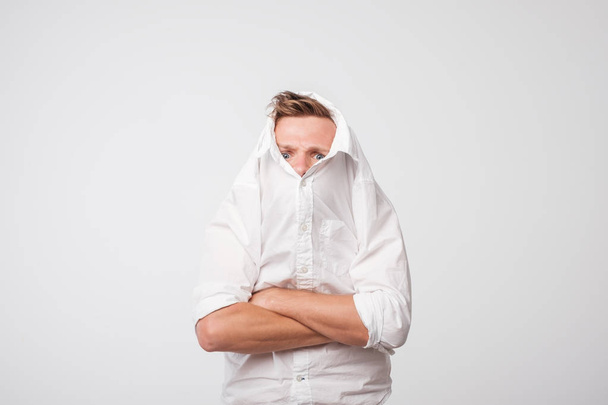 Angry caucasian man pulls a white shirt over his head. loneliness of depressed person. - Photo, Image