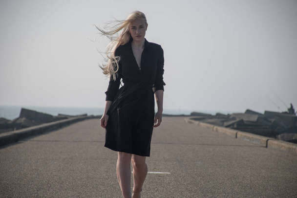 桟橋で黒いコートでブロンドの女の子 - 写真・画像