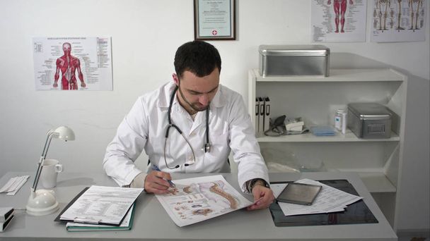 Physiotherapist in his practice, the vertebral column poster on his desk - Φωτογραφία, εικόνα