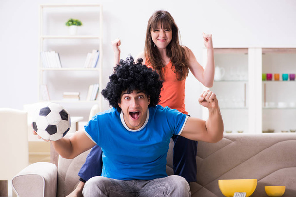 Молодой человек смотрит футбол с женой дома - Фото, изображение