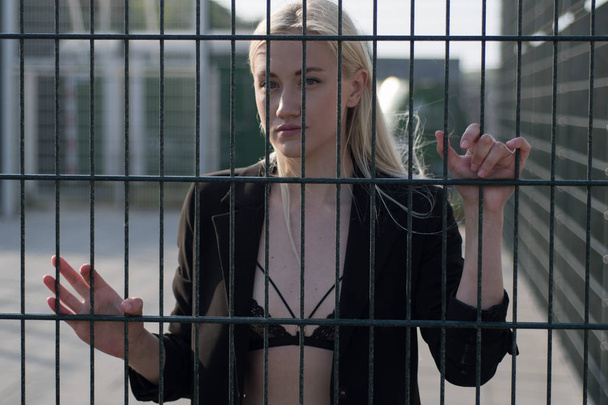 blonde fille dans un manteau noir derrière une clôture en métal
 - Photo, image