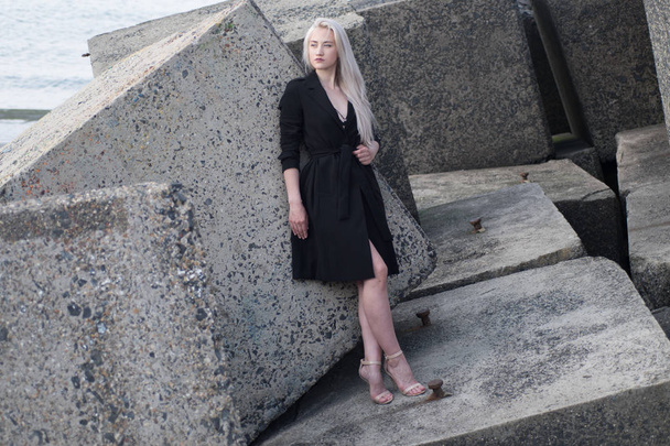 ξανθιά κοπέλα στο μαύρο παλτό στις πέτρες - Φωτογραφία, εικόνα