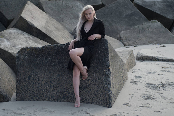  blonde girl in black coat on stones - Φωτογραφία, εικόνα