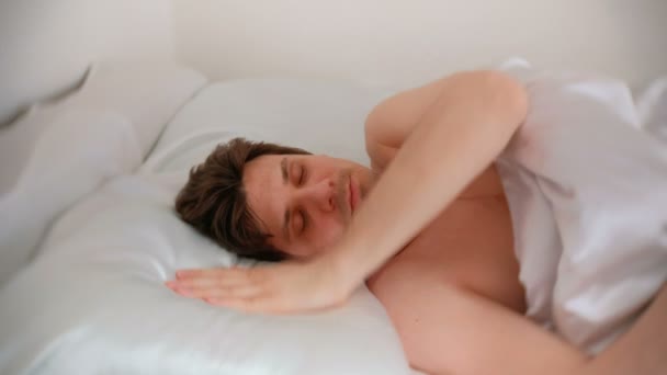 Young brunet handsome man wakes up and turns off the alarm on his mobile phone. - Záběry, video