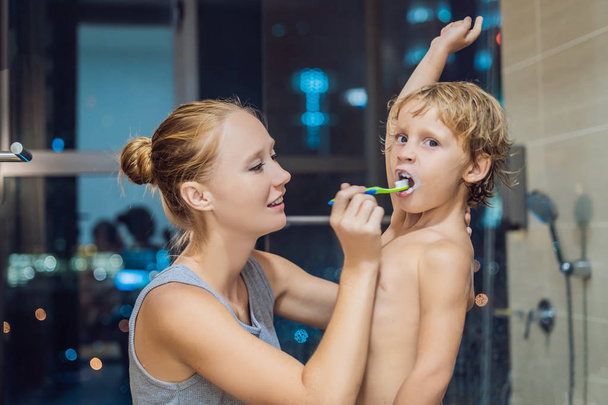 Mama czyści zęby jego syn przed pójściem spać na tle miasta w nocy. - Zdjęcie, obraz