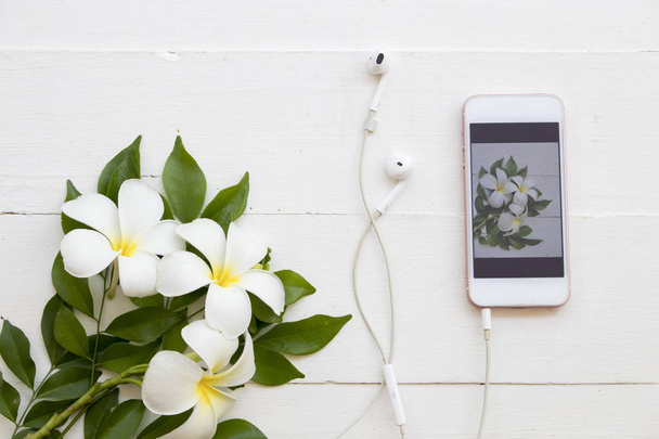 mobile phone with white flower frangipani arrangement on background white wooden - Zdjęcie, obraz