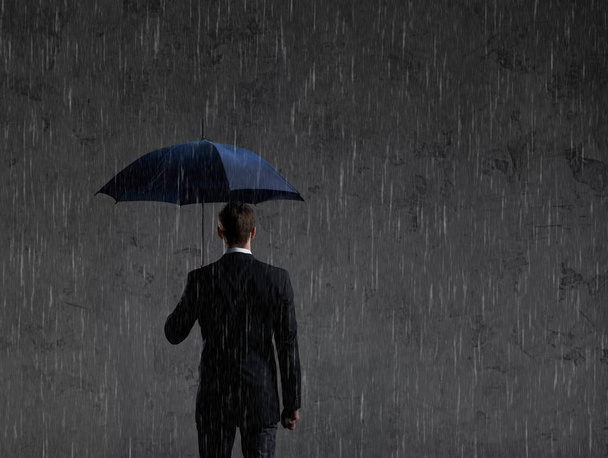 Businessman with umbrella standing under the rain. Dark, dramatic background. Business, failure, crisis concept  - Photo, image
