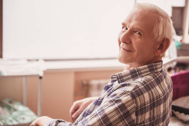 Beau vieil homme regarde la caméra et sourit tout en étant assis en fauteuil roulant dans la salle d'hôpital
 - Photo, image